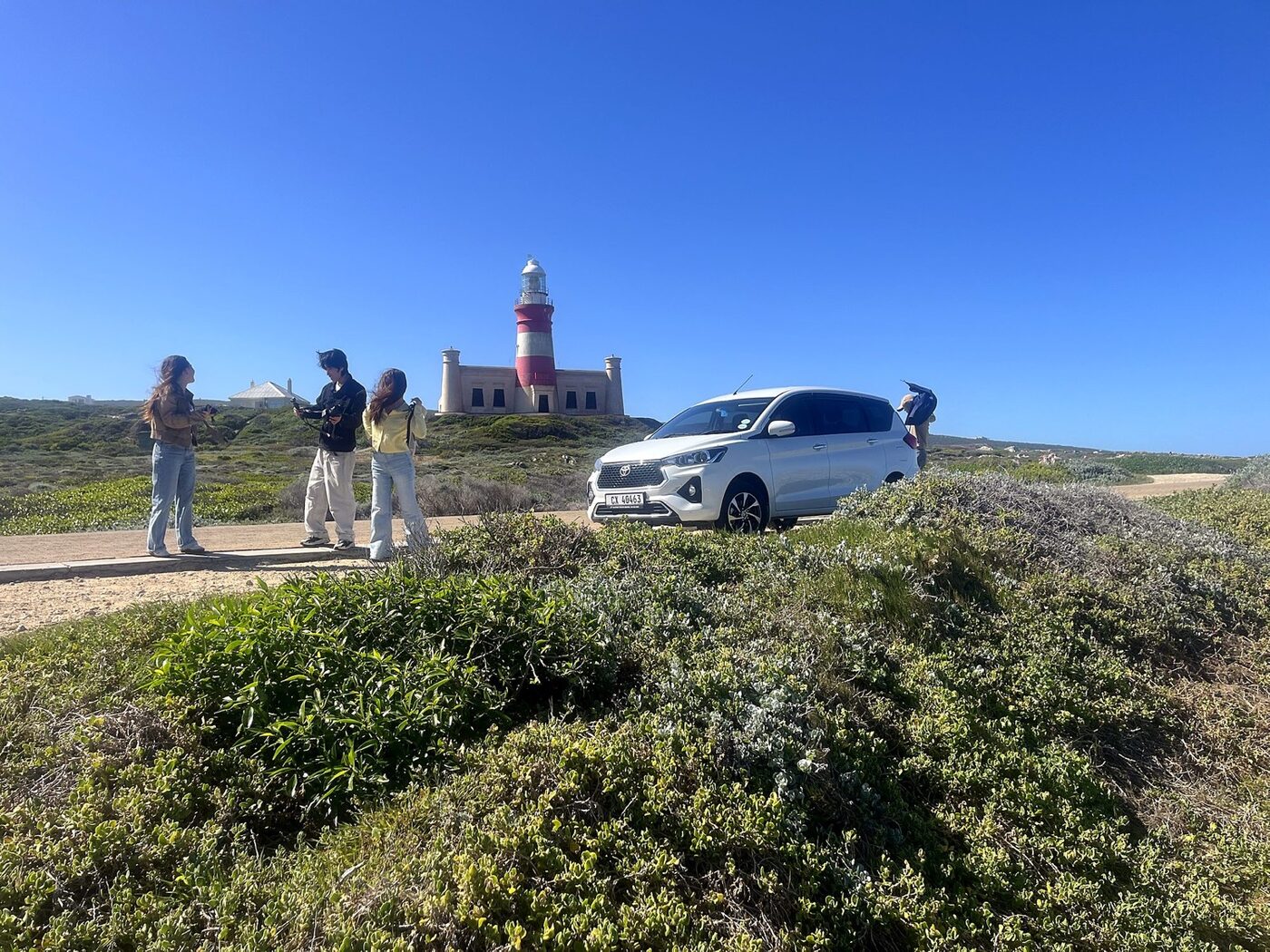 Toyota Rumion parked near the red-and-white Cape Agulhas lighthouse with guests