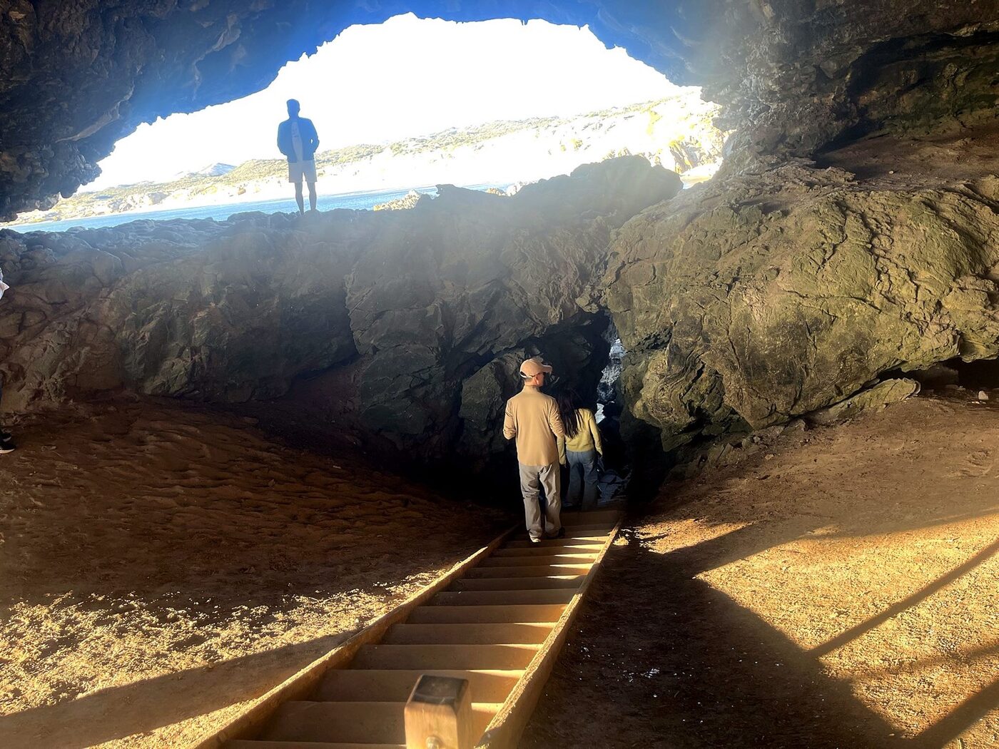 Walkers descending wooden steps inside Klipgat Cave toward the ocean light
